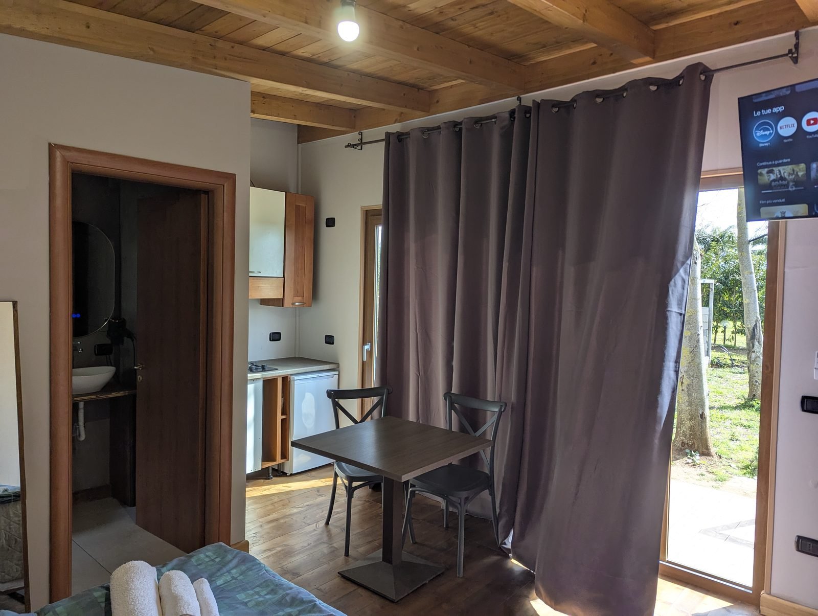 Interno del bungalow con angolo cottura, porta del bagno privato, tavolo per due e televisore