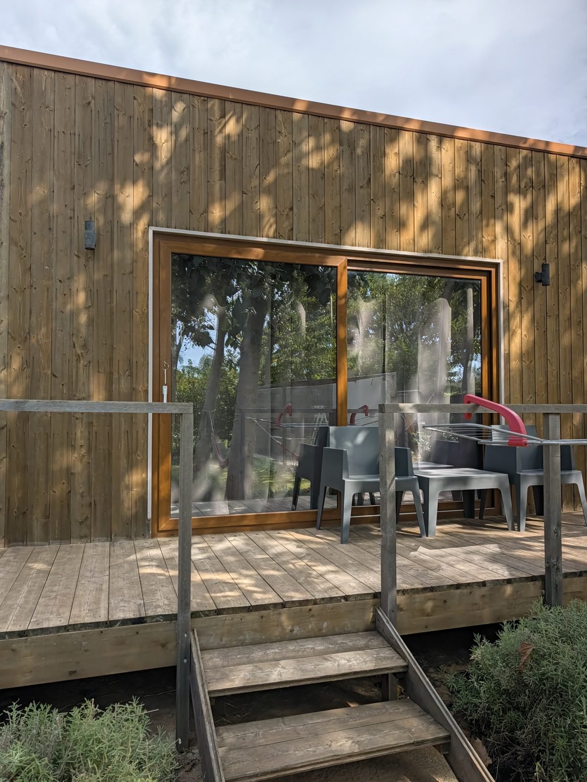 Terrazza in legno di un bungalow Cubo House con grande vetrata scorrevole e tavolo all'aperto