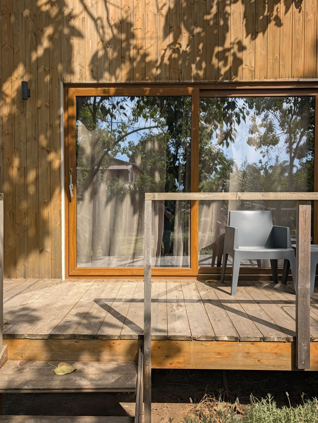 Vetrata e terrazza in legno del bungalow in controluce, con le ombre degli alberi